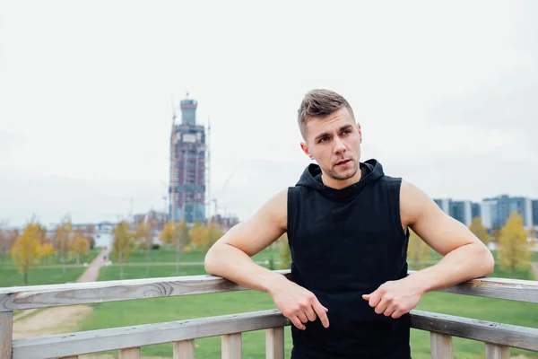 Sport fitness mężczyzna pozowanie na tle miasta. Sportowca poza upadek park. Dopasowanie modelu. — Zdjęcie stockowe