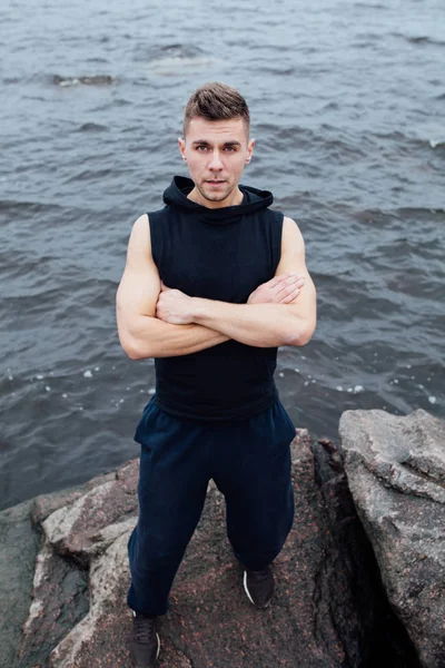 Starka yang fitness man poserar på stranden nära havet och klipporna. — Stockfoto