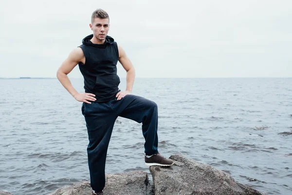 Yang silny człowiek fitness pozuje na plaży w pobliżu morze i skały. — Zdjęcie stockowe