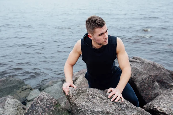 Stark man agerar yoga på stenar stranden på morgonen mot havet. — Stockfoto