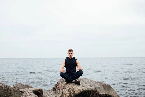 Stark fitness yoga mannen i lotus pose på rock stranden nära havet. Harmonisk koncept. — Stockfoto