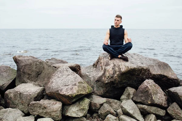 Silne fitness joga człowiek w pozycji lotosu na skalistej plaży, w pobliżu oceanu. Koncepcja harmonicznych. — Zdjęcie stockowe