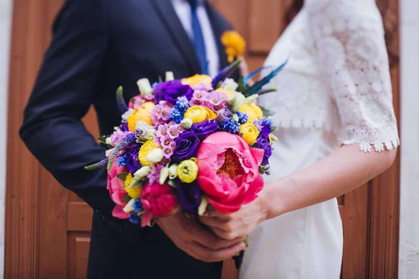 Nevěsta a ženich drží svatební kytici společně, venku. Láska. — Stock fotografie