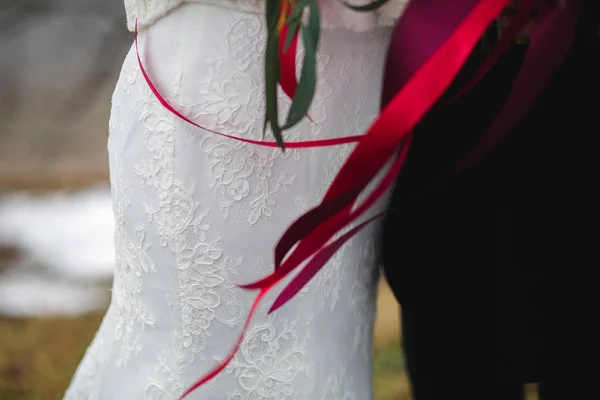 Nevěsta a ženich drží svatební kytici spolu s páskou, mimo — Stock fotografie
