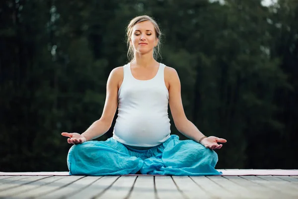 Genç kadın lotus pozisyonunda Nehri yanındaki ormanda yoga pratiği yapıyor. ahşap iskele paspaslar üzerine oturan. — Stok fotoğraf