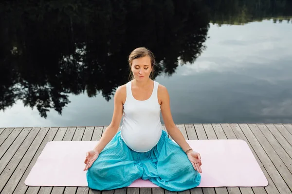 Genç kadın lotus pozisyonunda Nehri yanındaki ormanda yoga pratiği yapıyor. ahşap iskele paspaslar üzerine oturan. — Stok fotoğraf