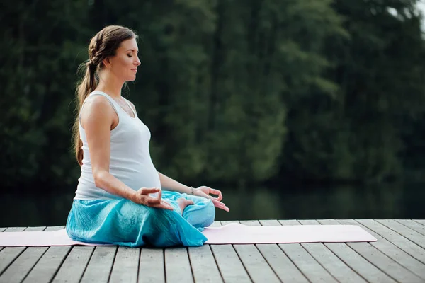 Genç kadın lotus pozisyonunda Nehri yanındaki ormanda yoga pratiği yapıyor. ahşap iskele paspaslar üzerine oturan. — Stok fotoğraf