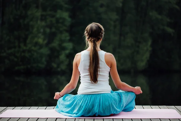 Genç kadın lotus pozisyonunda Nehri yanındaki ormanda yoga pratiği yapıyor. ahşap iskele paspaslar üzerine oturan. — Stok fotoğraf