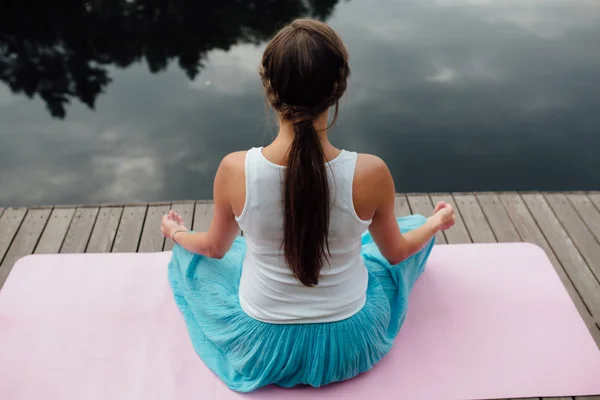 Genç kadın lotus pozisyonunda Nehri yanındaki ormanda yoga pratiği yapıyor. ahşap iskele paspaslar üzerine oturan. — Stok fotoğraf