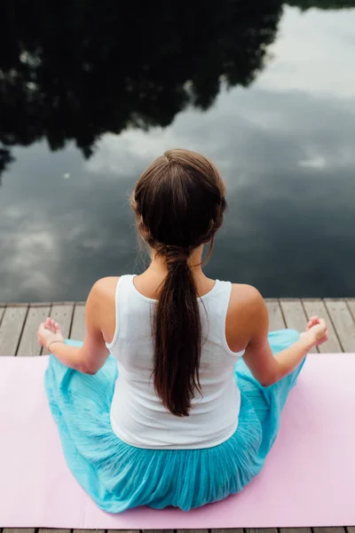 Genç kadın lotus pozisyonunda Nehri yanındaki ormanda yoga pratiği yapıyor. ahşap iskele paspaslar üzerine oturan. — Stok fotoğraf