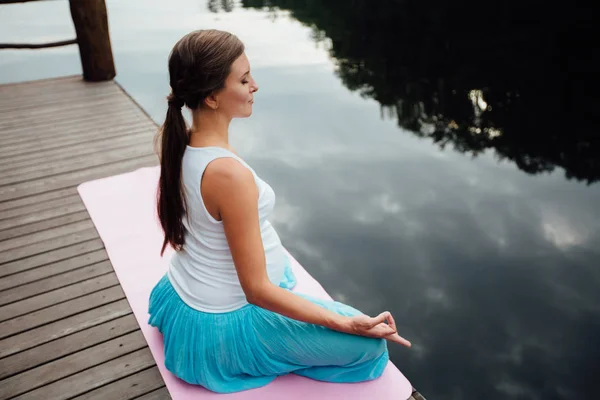 Genç kadın lotus pozisyonunda Nehri yanındaki ormanda yoga pratiği yapıyor. ahşap iskele paspaslar üzerine oturan. — Stok fotoğraf