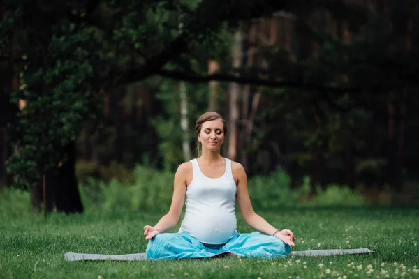 Hamile yoga orman arka plan üzerinde lotus olarak. parkta çim paspas, açık, Sağlık kadın. — Stok fotoğraf