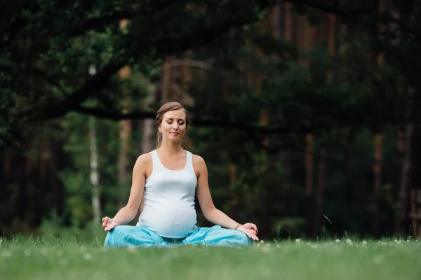 Hamile yoga orman arka plan üzerinde lotus olarak. parkta çim paspas, açık, Sağlık kadın. — Stok fotoğraf