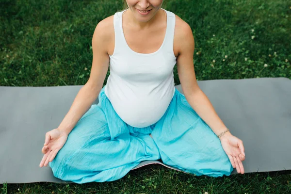 Yoga embarazada en la posición de loto en el fondo del bosque. en el parque la alfombra de hierba, al aire libre, mujer de la salud . — Foto de Stock