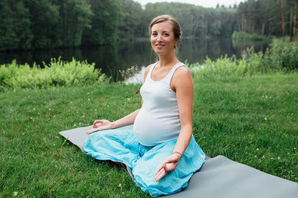 Lotus pozisyonu ve orman amd nehir arka plan üzerinde hamile yoga. parkta çim paspas, açık, Sağlık kadın. — Stok fotoğraf