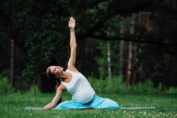 Беременная йога в позе лотоса на фоне леса. в парке коврик для травы, открытый, женщина здоровья . — стоковое фото