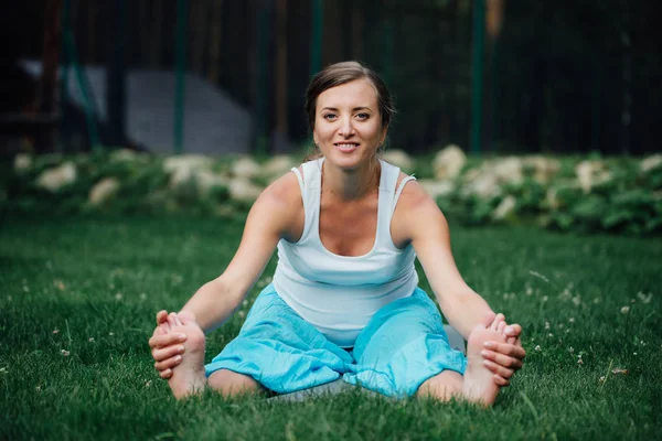Беременная йога в позе лотоса на фоне леса. in the park the grass, outdoor, health woman . — стоковое фото