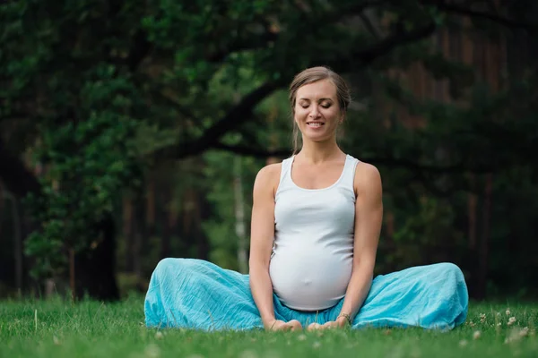 Yoga embarazada en posición de loto en el bosque entre el fondo del río. en el parque la hierba, al aire libre, mujer de la salud . — Foto de Stock