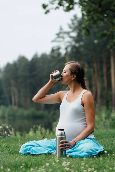 Yoga embarazada en posición de loto con termos bebiendo té. en el parque en la hierba, al aire libre, mujer de la salud, mujer . — Foto de Stock