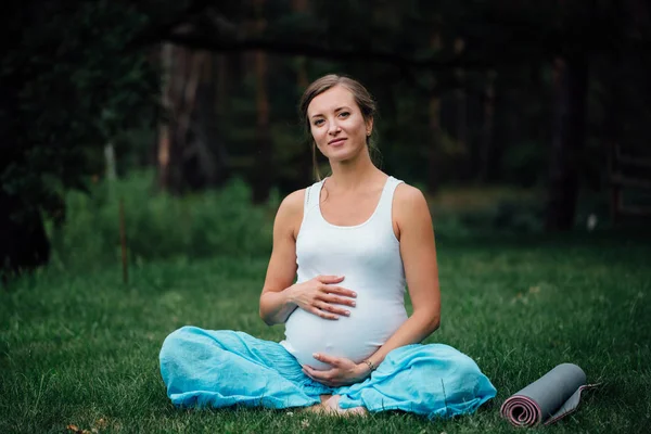 Mujer embarazada de yoga con retrato de estera en el parque sobre la hierba, respiración, estiramiento, estática. al aire libre, bosque . — Foto de Stock