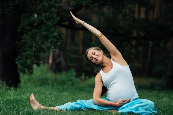 Maternidad prenatal de yoga embarazada haciendo diferentes ejercicios. en el parque en la hierba, respiración, estiramiento, estática . — Foto de Stock