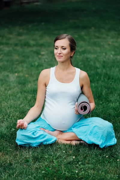Mujer embarazada de yoga en posición de loto con retrato de esterilla en el parque sobre la hierba, respiración, estiramiento, estática . — Foto de Stock