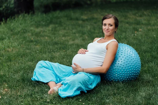 Embarazada de yoga prenatal haciendo diferentes ejercicios con fitball. en el parque en la hierba, respiración, estiramiento, Pilates . — Foto de Stock