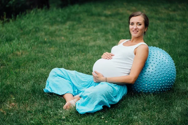 Embarazada de yoga prenatal haciendo diferentes ejercicios con fitball. en el parque en la hierba, respiración, estiramiento, Pilates . — Foto de Stock