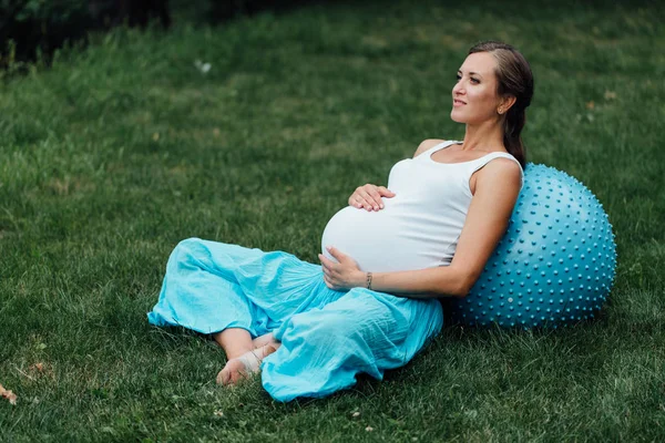 Embarazada de yoga prenatal haciendo diferentes ejercicios con fitball. en el parque en la hierba, respiración, estiramiento, Pilates . — Foto de Stock