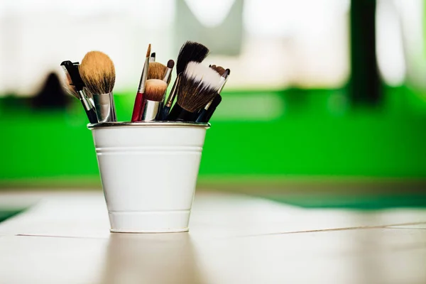 Várias escovas de maquiagem e lápis no fundo verde claro dentro do balde no chão. espaço de cópia — Fotografia de Stock