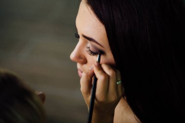 Parlak temel renk modelleri yüzünde uygulama ve bir fırça tutan kalıcı makyaj sanatçı el kapatın .