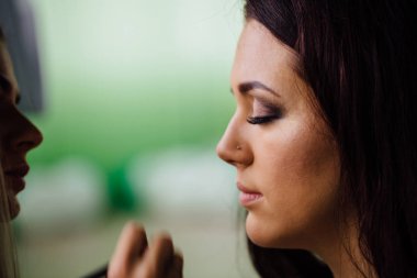 Parlak temel renk modelleri yüzünde uygulama ve bir fırça tutan kalıcı makyaj sanatçı el kapatın .