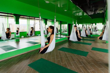 young women making antigravity yoga exercises with a group of people. aero fly fitness trainer workout. white hammocks. clipart
