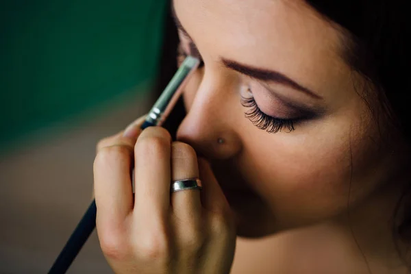 Maquiagem mão artista aplicando cor base brilhante no rosto modelos e segurando um pincel, perto  . — Fotografia de Stock