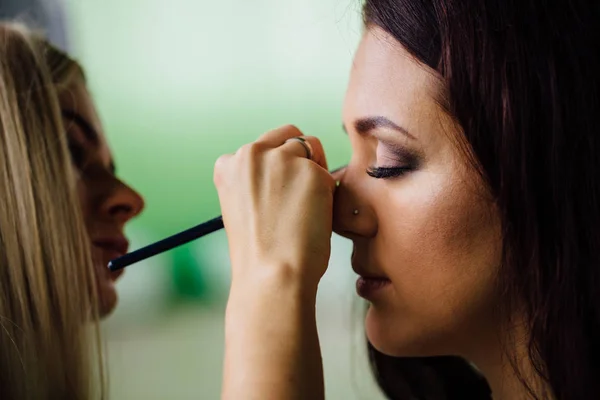 Maquiagem mão artista aplicando cor base brilhante no rosto modelos e segurando um pincel, perto  . — Fotografia de Stock