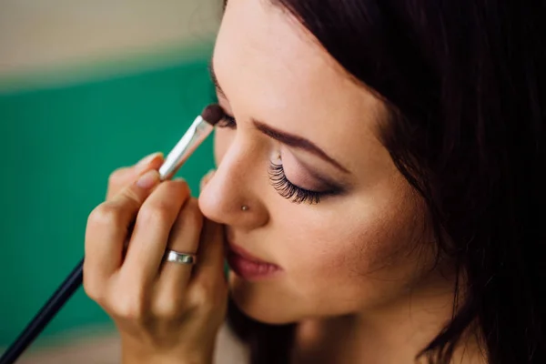 Maquiagem mão artista aplicando cor base brilhante no rosto modelos e segurando um pincel, perto  . — Fotografia de Stock