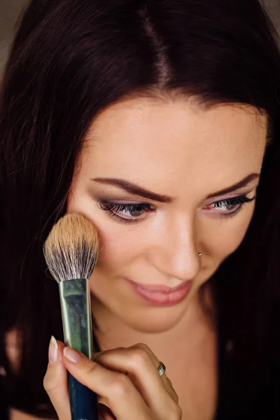 Maquiagem mão artista aplicando cor base brilhante no rosto modelos e segurando um pincel, perto  . — Fotografia de Stock