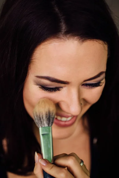 Maquillaje artista mano aplicando color base brillante en la cara de los modelos y sosteniendo un cepillo, cerca  . — Foto de Stock