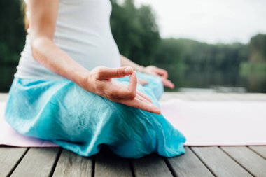 Lotus pozisyonu closeup meditasyon kadın. Yakın çekim mudra eller. Nehir kıyısında ahşap zemin üzerinde oturan