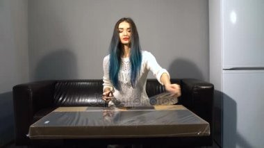 Bir tablo bir araya genç sevimli kız renkli saçlı yeni apartmanda bir kanepede oturuyor. Mutfakta ateş. paket makasla paketini açmalısınız.
