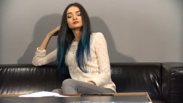 Joven linda chica con el pelo de color sentado en un sofá en su nuevo apartamento para armar una mesa. Dispara en la cocina . — Vídeos de Stock