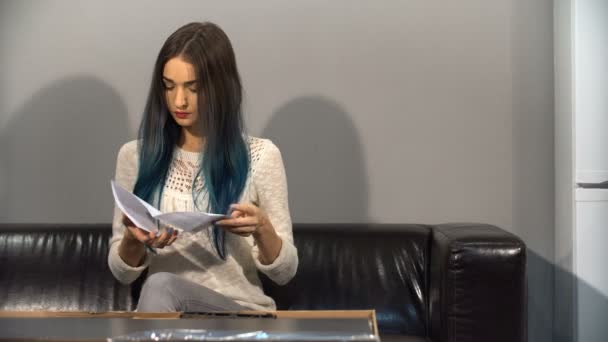 Joven linda chica con el pelo de color sentado en un sofá en su nuevo apartamento para armar una mesa. Dispara en la cocina . — Vídeos de Stock