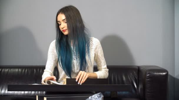 Молодая милая девушка с цветными волосами, сидящая на диване в своей новой квартире, чтобы собрать стол. Съемки на кухне . — стоковое видео