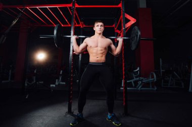 spor salonunda yakışıklı bir atlet portresi. adam egzersiz halter, ayakta ve çömelme ile yapar. büyük emin