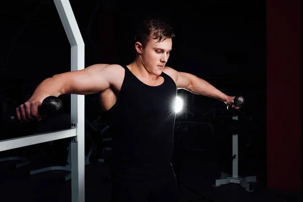 Retrato de un joven musculoso levantando pesas sobre el fondo del gimnasio. Ejercitar los hombros —  Fotos de Stock