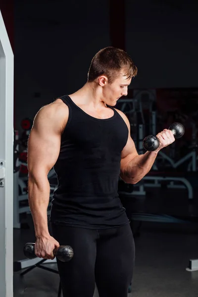Portret van een gespierde jonge man tillen gewichten op gym achtergrond. — Stockfoto