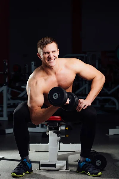 professional bodybuilder do exercises for biceps sitting on the bench, with dumbbells at gym. Big