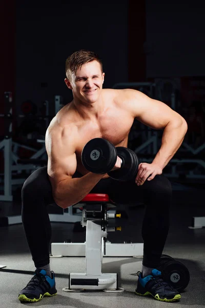 professional bodybuilder do exercises for biceps sitting on the bench, with dumbbells at gym. Big