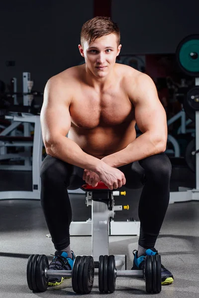 Culturista profesional sentado en el banco, descansando entre ejercicios con pesas en el gimnasio. Grande. —  Fotos de Stock