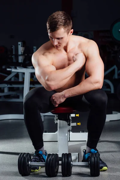 Bodybuilder fitness professionnel assis sur le banc et démontre les muscles de votre corps après une séance d'entraînement, à la salle de gym . — Photo